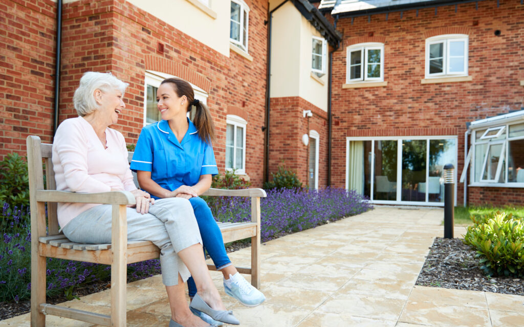 Care professional and older resident sharing a conversation outdoors at a care home